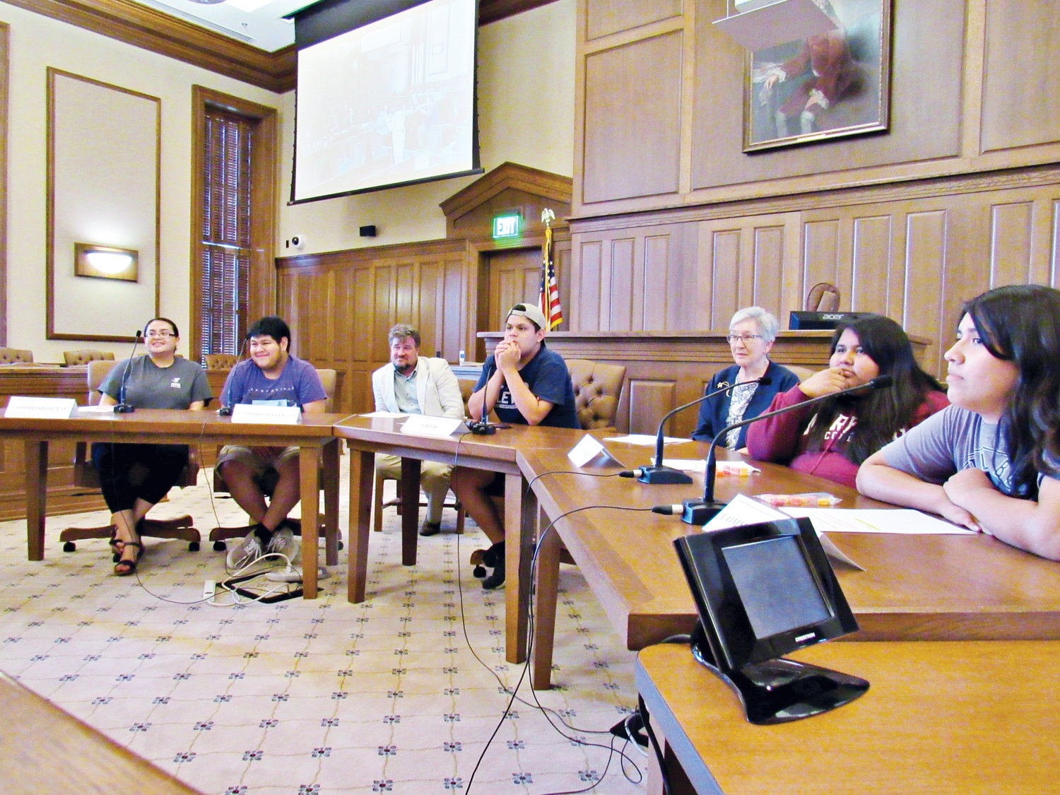 picture of 6 latinx youth and two county commissioners sitting in the commissioner chairs in the historic court house